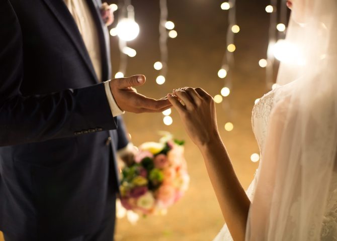Evening wedding ceremony. The bride and groom holding hands on a background of lights and lanterns.